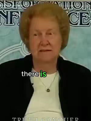 A woman with short, reddish-blonde hair is centered in the frame, looking straight ahead. The background is slightly out of focus, but appears to be a banner or sign. Below her is a text overlay that says, 'there is' in green. At the bottom of the frame is more text that reads 'TRUTH CONQUER'. She is wearing a black blazer over a white top, and a small necklace.
