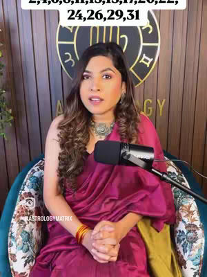 A woman sits in a decorative chair, speaking. She is wearing a maroon top with gold and orange jewelry and a detailed top.
