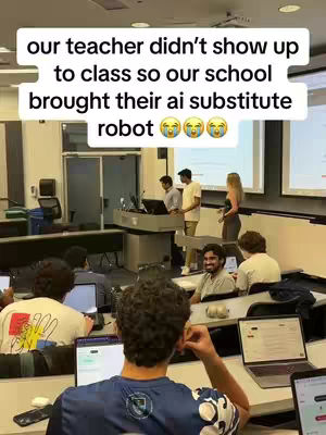 The image shows a medium shot of a college classroom. Several students are seated at desks with laptops, the foreground filled with the backs of students' heads. In the middle ground, several figures are near a podium, and a screen displays a presentation. The text overlayed says that the teacher did not show up and their school brought an AI substitute robot.