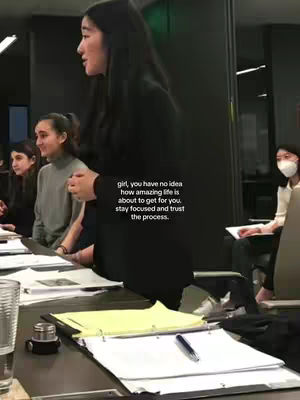 A young woman stands in what appears to be an office setting, addressing a group. She's the main focus, with others in the background. Text overlays a motivational message, set against a neutral-toned environment.