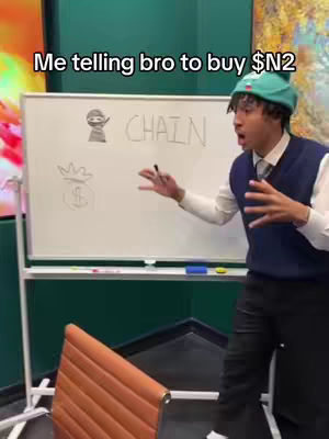 A man in a teal beanie and vest gestures in front of a whiteboard, with the text "Me telling bro to buy $N2" as overlay. The whiteboard has drawings related to money and the word "CHAIN."