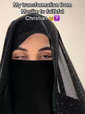 A close-up shot features a woman's face partially covered by a black veil with small, scattered white sparkles. Her eyes are visible above the veil, and she gazes slightly to the side. The background is plain and indistinct.