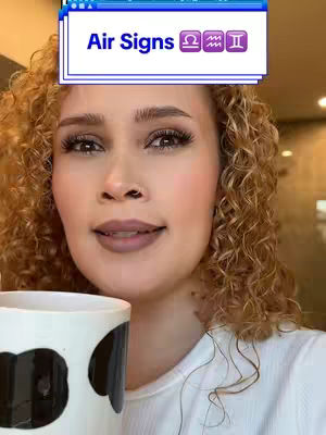 A medium shot of a woman with curly blonde hair. She holds a large mug with a black and white pattern. The woman has light makeup, and a text overlay at the top of the frame displays the text "Air Signs" along with three astrological symbols. The background is out of focus.
