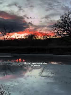 A landscape view featuring a reflective body of water in the foreground. Above, a vibrant sunset paints the sky with shades of red, orange, and gray, contrasted by dark silhouettes of trees and clouds. The text overlay reads 'I found peace in knowing your mine.'
