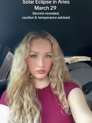A woman with long, wavy blonde hair and makeup looks somberly at the camera. Text overlays read, "Solar Eclipse in Aries March 29 Secrets revealed, caution & temperance advised."