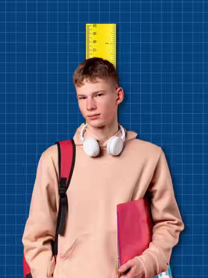A young man with short brown hair and a friendly expression stands in front of a blue grid background. He wears a light brown hoodie, white headphones around his neck, and a red backpack. He holds a red file folder. A yellow ruler is digitally overlaid above his head.