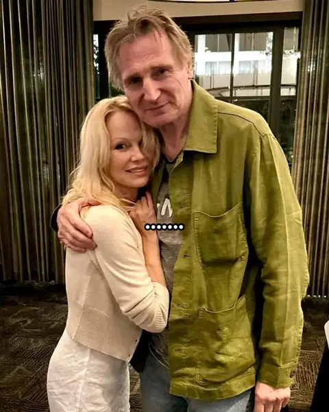 The cover image features a photo of Pamela Anderson with Liam Neeson, both smiling and embracing each other. The background includes room decor. Colors are natural, with neutral tones.