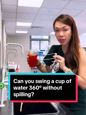 A woman stands in a lab setting, holding a cup of red liquid. A text overlay asks if one can swing a cup of water 360 degrees without spilling. The background includes lab equipment and sinks.