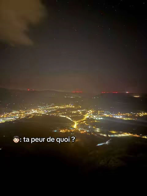 A night landscape shot from a high angle of a city with many lights. Above, the sky transitions from dark to cloudy with some visible stars. In the foreground, there is a text overlay with an emoji.
