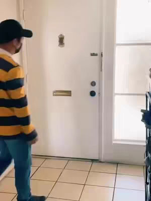 A person in a striped shirt and a cap is walking on the left. The person is walking toward a white door on the right side of the frame.