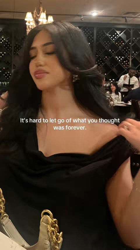 A woman in a black dress is the central focus, positioned slightly off-center. She is in a restaurant setting. The cover image displays a woman with long, dark hair, wearing a black dress that exposes her shoulders. She seems to be in a restaurant environment, with a blurred background showing tables and other people. The lighting appears to be a mix of natural and artificial.