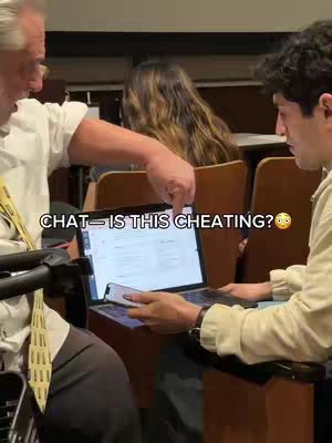 An interior shot of a classroom with a man pointing to a laptop screen. A younger man to the right is looking at the screen, and there's a woman in the background. The words 'CHAT - IS THIS CHEATING?' are superimposed on the image.