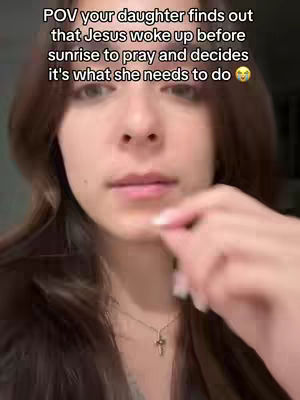 A selfie-style shot featuring a young woman. The foreground shows her face in close-up, with her hair framing her face and a delicate cross necklace visible. Text overlay adds context. The background is intentionally out of focus, emphasizing the subject.