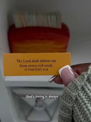 A close-up shot shows a hand holding a yellow card with text against a blurred background. The card has a Bible verse and the hand has manicured nails.