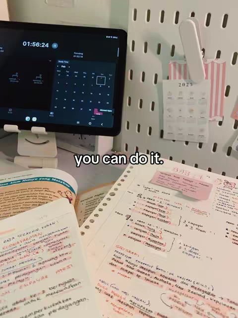 The image shows a study setup with a tablet displaying a calendar, open notebooks filled with handwritten notes, and a whiteboard with a calendar. The lighting appears to be from a natural source, creating a clear and well-lit environment. The color palette is dominated by neutral tones, making the written content easily readable. The composition is organized, with study materials arranged for focus and effective learning.