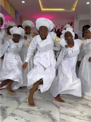 A group of people in white outfits and matching hats dancing in a well-lit room with a marble patterned floor. The composition is dynamic with the dancers in mid-step.