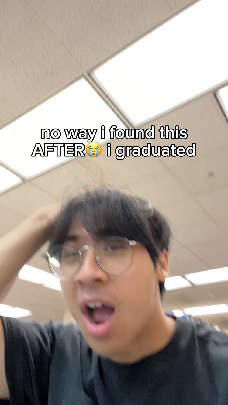 A young man with dark hair and glasses is shown in a close-up, slightly angled shot. He has an open mouth and a hand raised towards his hair, with an expression of surprise or dismay. Bold white text overlays the image, reading "no way i found this AFTER i graduated". The background is a plain, off-white ceiling with recessed lighting.