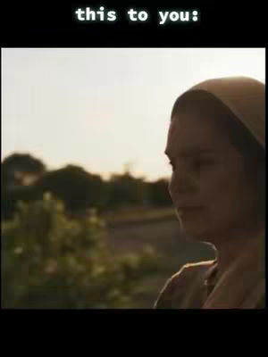 A woman in simple attire stands outdoors, her head turned to the side. The lighting is soft, and the background is blurred, giving the image a serene and introspective mood.