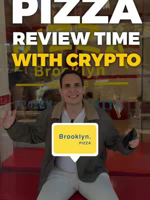 A man is in front of a pizza shop with overlaid text. The man is smiling wearing a jacket and white shirt. The text overlays are white and yellow and the background is the pizza shop.