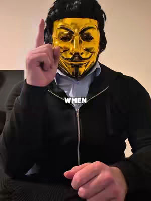 A person wearing a gold Guy Fawkes mask, pointing their index finger upwards. They are wearing a black jacket with a white dress shirt and partially unbuttoned. The text overlay 'WHEN' is placed near the middle of the image.