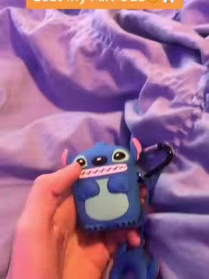 A hand holds a Stitch-themed AirPod case, set against a purple, wrinkled fabric background. The case is blue with Stitch's features, and the text 'Lost my AirPod?!' is overlaid on the top.