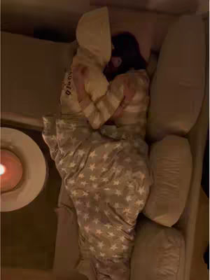 An overhead shot of a couple cuddled together on a couch. They are covered with a blanket featuring a star pattern. A small table with a lit candle is visible in the corner.