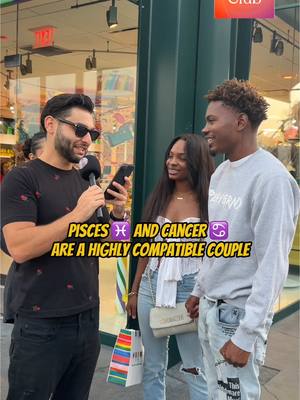 An outdoor scene captures three people on a sunny day. The main subject, a man with a beard and sunglasses, holds a microphone and a phone, looking at the screen. To his right stand a man wearing a gray sweatshirt, and a woman with long dark hair is to his left. The background includes storefronts, suggesting a street setting. Text overlaid on the image reads "PISCES ♓ AND CANCER ♋ ARE A HIGHLY COMPATIBLE COUPLE"