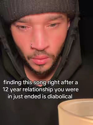 A close-up shot of a man with a beard and a beanie, his expression deeply sorrowful, with visible tears in his eyes. Text overlayed at the bottom provides context about a recent breakup.