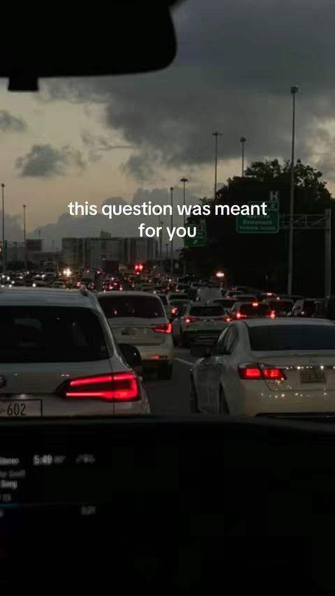 The cover image captures a view from inside a car stuck in heavy traffic at dusk. The sky is overcast, and the setting sun casts a muted glow on the scene. The foreground shows the car's interior elements, with other vehicles extending into the background. Overlaid text reads, 'this question was meant for you'. The overall composition has a somber, reflective tone.