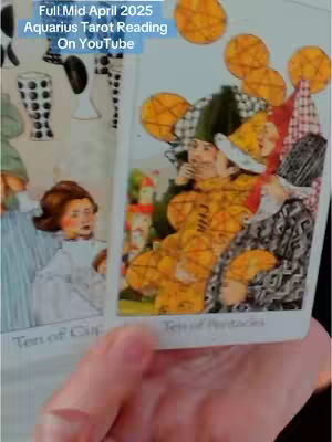 The image shows a hand holding two tarot cards. The text overlay at the top reads, 'Full Mid April 2025 Aquarius Tarot Reading On YouTube.' The card on the right has a yellow color scheme, with a figure in a patterned outfit and hat. The left card shows a lady in white dress.