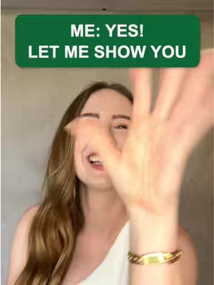 A woman with long, wavy brown hair is smiling and reaching forward with her right hand, appearing to be gesturing towards the viewer. She is wearing a white top and a gold bracelet. Above her head is a green rectangle with white text that reads "ME: YES! LET ME SHOW YOU". The background is a neutral, blurry gradient.