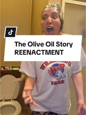 The cover image shows a person, likely female, with what appears to be oil or some kind of liquid on their head and face, with wide eyes and an open mouth conveying shock or surprise. The person is wearing a t-shirt with a logo. In the background is a bathroom setting with a toilet and a door. Text overlayed says "The Olive Oil Story REENACTMENT."