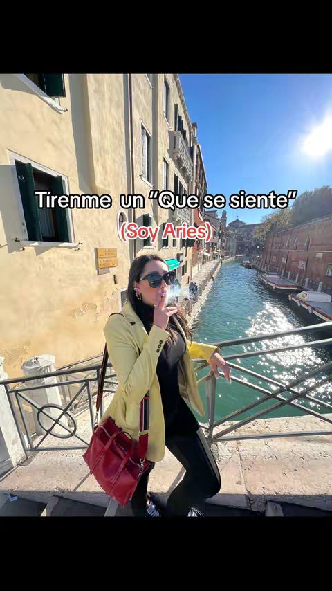 A woman stands near a canal with buildings in the background, smoking a cigarette. Text overlays are present.