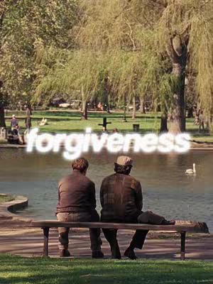 Two men sit on a park bench, facing away from the camera towards a lake. The background features a lush green park with trees, a pond, and a few people in the far distance. The text overlayed on the image reads 'forgiveness'.