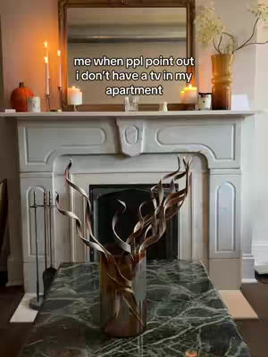 The cover image shows a room interior with a white fireplace mantel. On the mantel are candles, a mirror, and decorative items. A large vase with a unique artistic design is placed on a table in front of the fireplace.