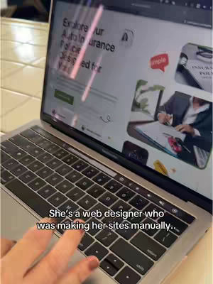 The video shows a laptop displaying a website interface, with a hand pointing towards the keyboard. The overlay text reads 'She's a web designer who was making her sites manually...'. The background displays a wooden surface providing context of the laptop's setting, likely indoors. The screen showcases a design related to auto insurance.