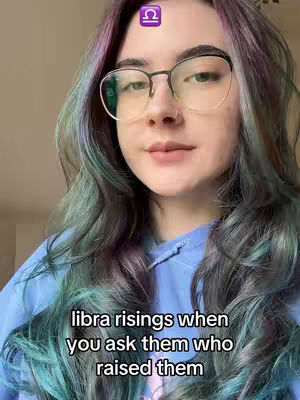 A young woman with long, multi-toned hair and glasses is centered in a selfie-style shot. The background seems to be a neutral, soft beige or light brown. She is wearing a blue hoodie. The text overlay is at the bottom and reads: 'libra risings when you ask them who raised them.' In the upper part of the image is a Libra zodiac symbol.