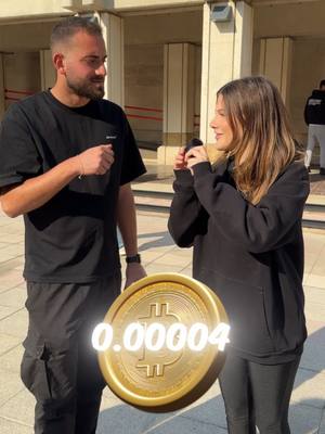 Two people are standing in front of a building. A large, golden bitcoin coin with the value 0.00004 is superimposed in the foreground. The text '1 Bitcoin saret $100,000' is overlaid on the image.