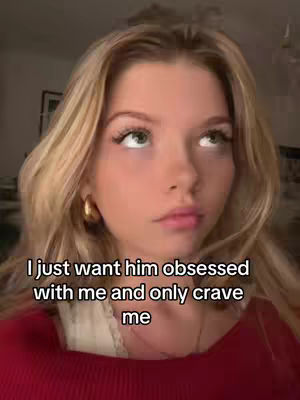 A close-up shot of a young woman with long, blonde hair and a red top looking upwards with a thoughtful expression. Text overlayed states, "I just want him obsessed with me and only crave me."