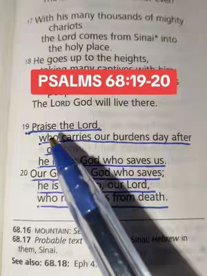 An open book displaying a Bible verse. Accompanying the text is a red rectangular box with the text: PSALMS 68:19-20. A blue pen is used to underline specific passages.