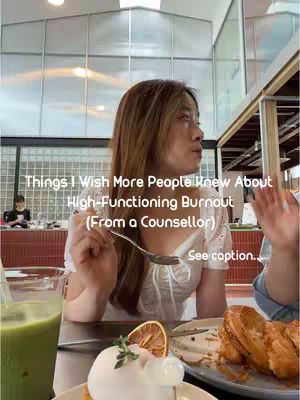 A young woman with long brown hair is seated at a table in a cafe. She is facing slightly to the left, holding a spoon near her face. On the table in front of her are a dessert and a partially visible glass of green liquid. The background blurs to show an open, modern cafe setting.
