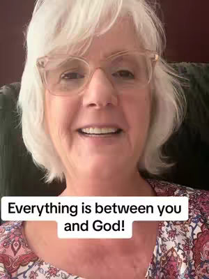 A selfie-style shot featuring a woman with white hair and glasses, smiling at the camera. A text overlay at the bottom reads: 'Everything is between you and God!' The background is blurred, suggesting an interior setting.