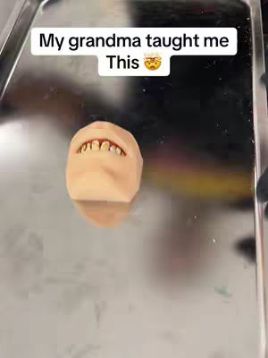 The cover image shows a close-up of a small, human-like sculpture of a mouth and teeth on a reflective metal surface. Above the sculpture, text reads, 'My grandma taught me this 😠'. The overall composition is simple, with the focus on the sculpture and text. The reflective surface creates depth.