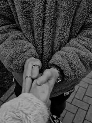 A black and white image focuses on two sets of hands intertwined. One hand is wearing rings. The subjects are wearing fuzzy jackets.