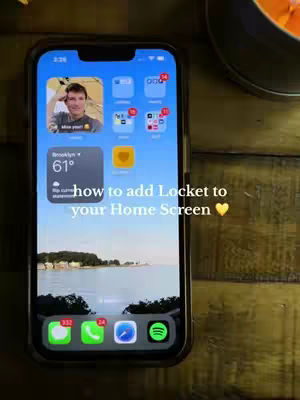 The cover image shows an iPhone displaying its home screen, with an image of a person in a locket widget. The screen also shows various app icons. Overlayed text is positioned at the bottom of the image, over a view of water and a distant shoreline, stating the video's purpose.