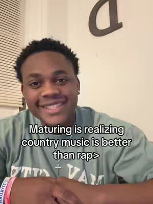 A young black man smiling at the camera in front of a plain wall with a stylized 'd' on it. He has short, dark hair. He is wearing a light green t-shirt with what appears to be a logo. The overlay text is black, clear and easy to read, centered in the bottom middle of the image