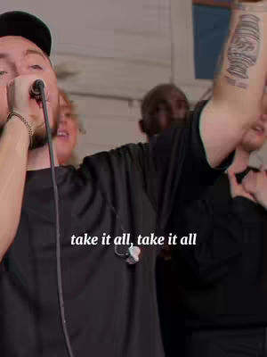 The cover image features a man singing into a microphone. The text overlay says "take it all, take it all". Multiple people are in the background, the lighting is bright, potentially reflecting a stage or performance setting. The predominant colors are black and white creating a contrast.