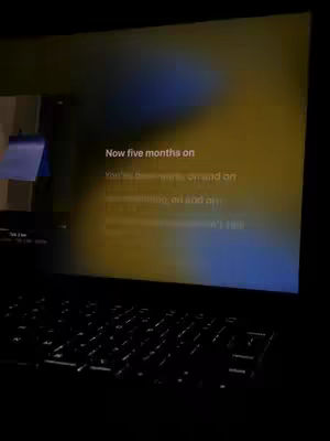 A laptop is open, displaying a screen with light yellow and blue gradients. Text overlays the gradient. The keyboard is in the foreground, underlit to give the whole scene a dark, moody feel.