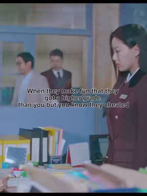 The image is a screenshot from a scene likely from kdrama, showing a girl in a maroon uniform standing in what appears to be an office setting. The foreground has a desk cluttered with files and office supplies. In the background, there are two men blurred slightly. The overall composition has a focus on the central female figure with text overlayed on her appearance.