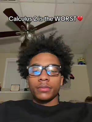 A selfie-style video cover features a young man with dark, curly hair and glasses. The background is simple and includes a ceiling fan and a portion of a window. Text overlaid on the image reads, "Calculus 2 is the WORST" with a red heart.